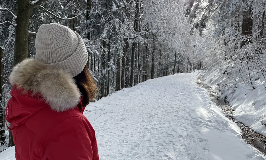 Cubea | Chalet-Apartments in Bodenmais für hohe Ansprüche Frau in rotem Mantel und Mütze wandert auf verschneitem Waldweg