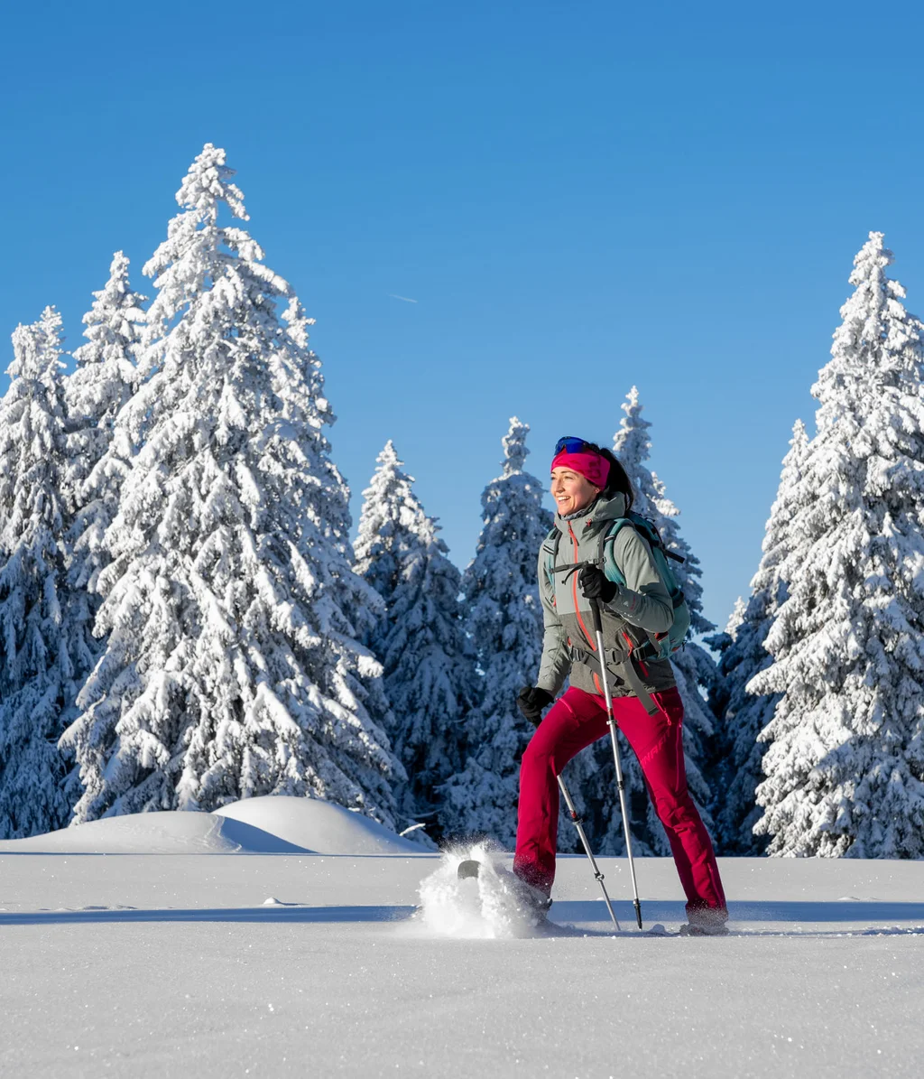 Cubea | Chalet-Apartments in Bodenmais für hohe Ansprüche Frau beim Schneeschuhwandern im verschneiten Wald bei klarem Himmel